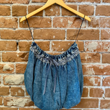 Blue denim dress with lace details on a wooden hanger against a brick wall.