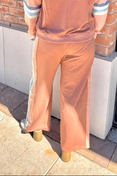 Person wearing a brown outfit standing against a brick wall.