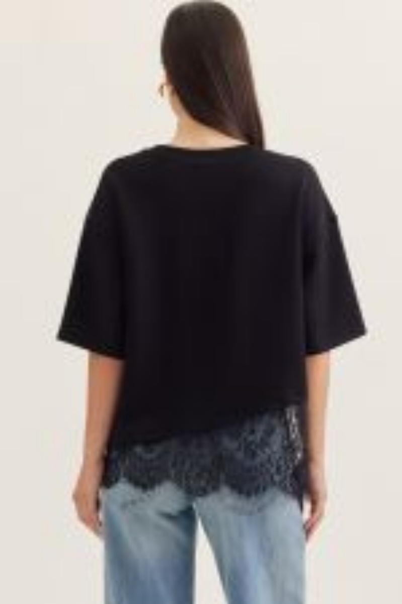 Person wearing a black oversized top with lace trim and light blue jeans on a plain background
