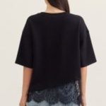 Person wearing a black oversized top with lace trim and light blue jeans on a plain background