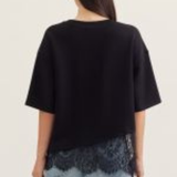 Person wearing a black oversized top with lace trim and light blue jeans on a plain background