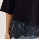 Person wearing a black top with lace trim and light blue jeans on a plain background