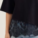 Person wearing a black top with lace trim and light blue jeans on a plain background
