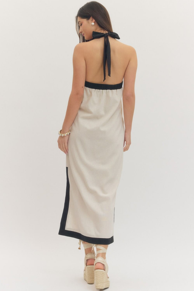 Woman wearing a beige halter neck dress with black trim on a white background