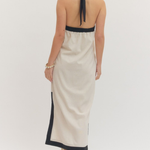 Woman wearing a beige halter neck dress with black trim on a white background