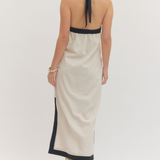 Woman wearing a beige halter neck dress with black trim on a white background