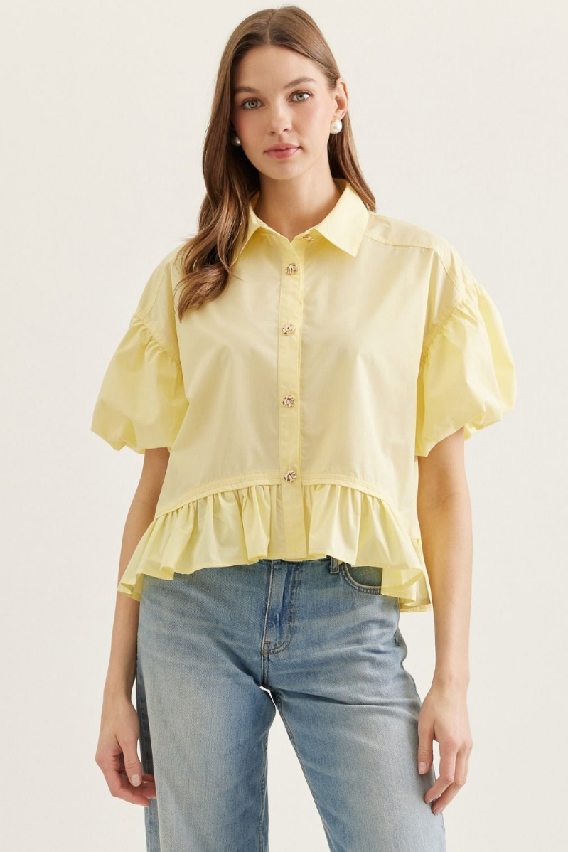Woman wearing a yellow blouse with ruffled sleeves and hem, standing against a plain background.