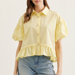 Woman wearing a yellow blouse with ruffled sleeves and hem, standing against a plain background.