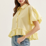 Woman wearing a yellow blouse with ruffled sleeves and hem on a white background
