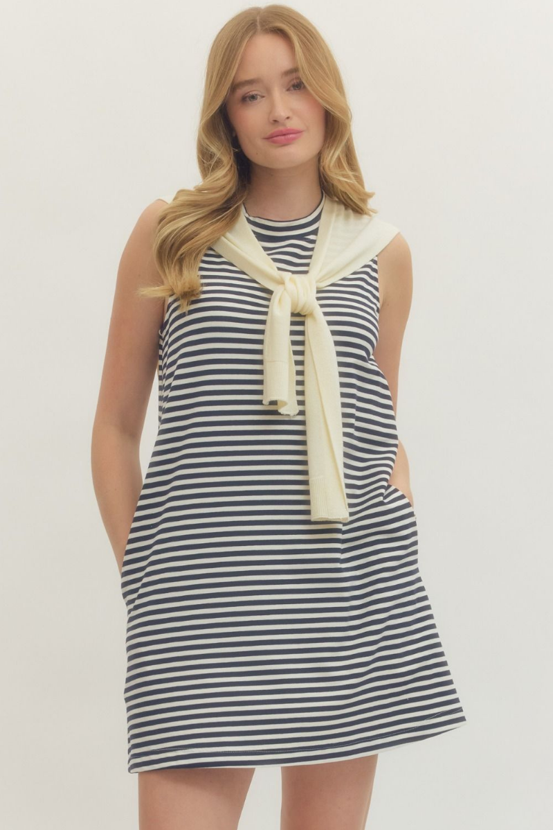 Woman wearing a striped dress with a yellow scarf on a plain background