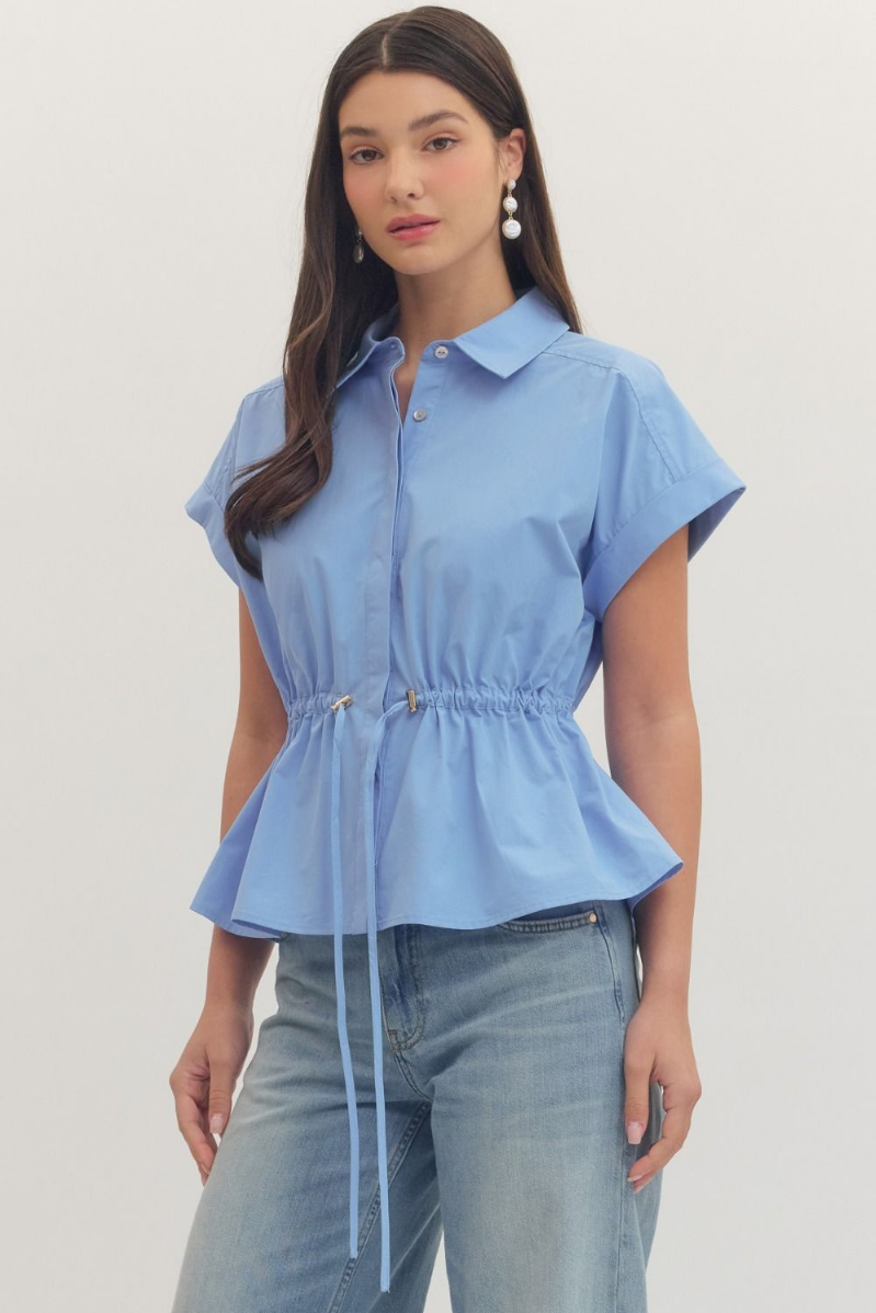 Woman wearing a light blue peplum top and jeans on a plain background