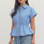 Woman wearing a light blue peplum top and jeans on a plain background