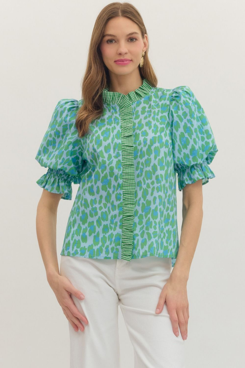 Woman wearing a green patterned blouse with white pants on a plain background