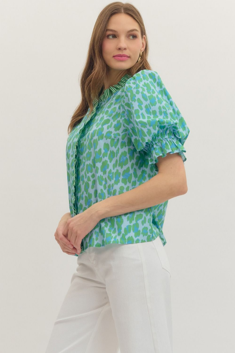 Woman wearing a green patterned blouse and white pants on a white background