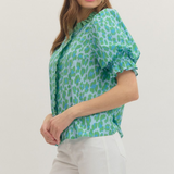 Woman wearing a green patterned blouse and white pants on a white background