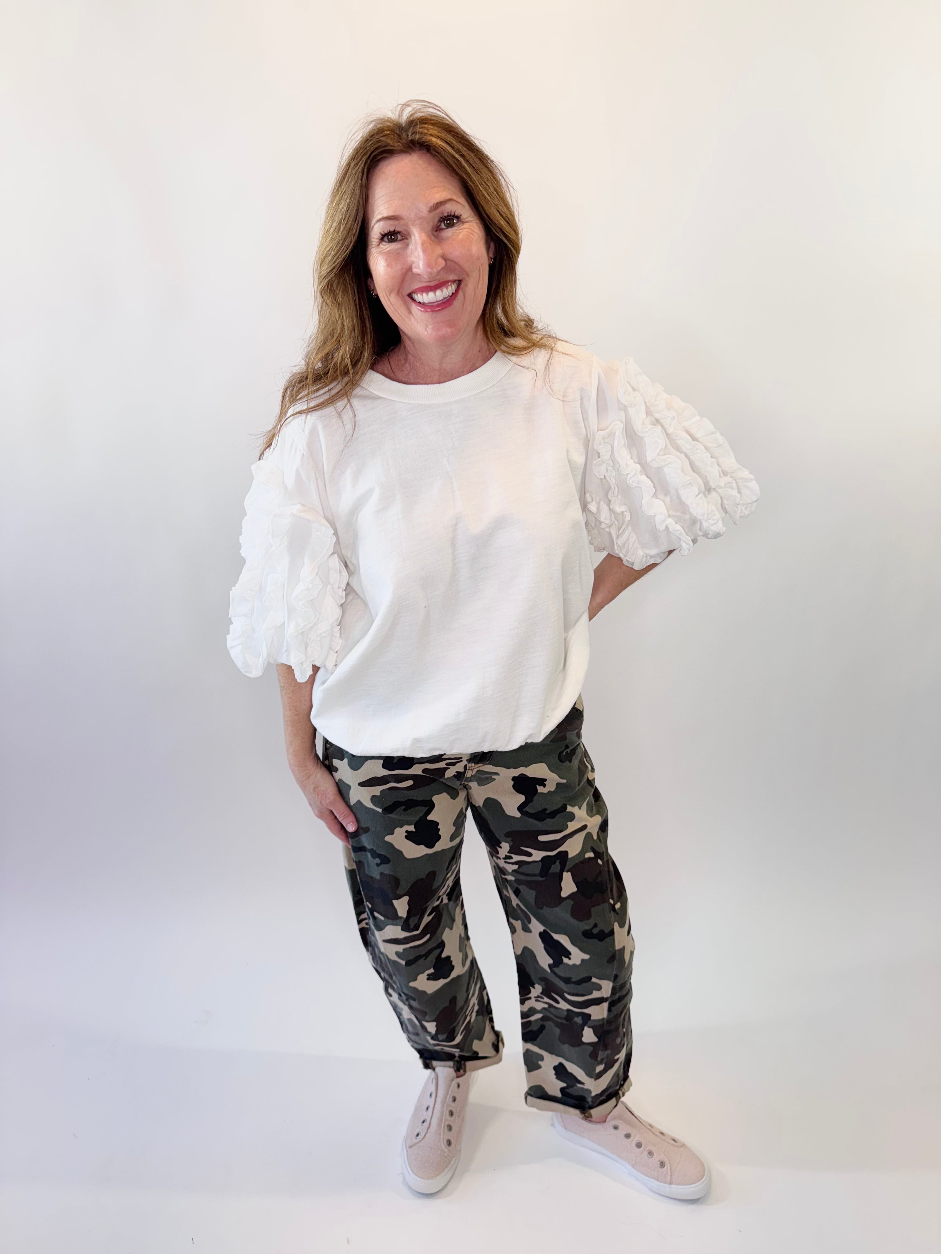 Woman wearing a white blouse with puff sleeves and camouflage pants on a white background