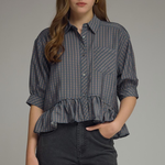 Woman wearing a checkered blouse with ruffled bottom and dark pants on a gray background