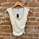 White sleeveless top on a hanger against a brick wall