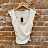 White sleeveless top on a hanger against a brick wall