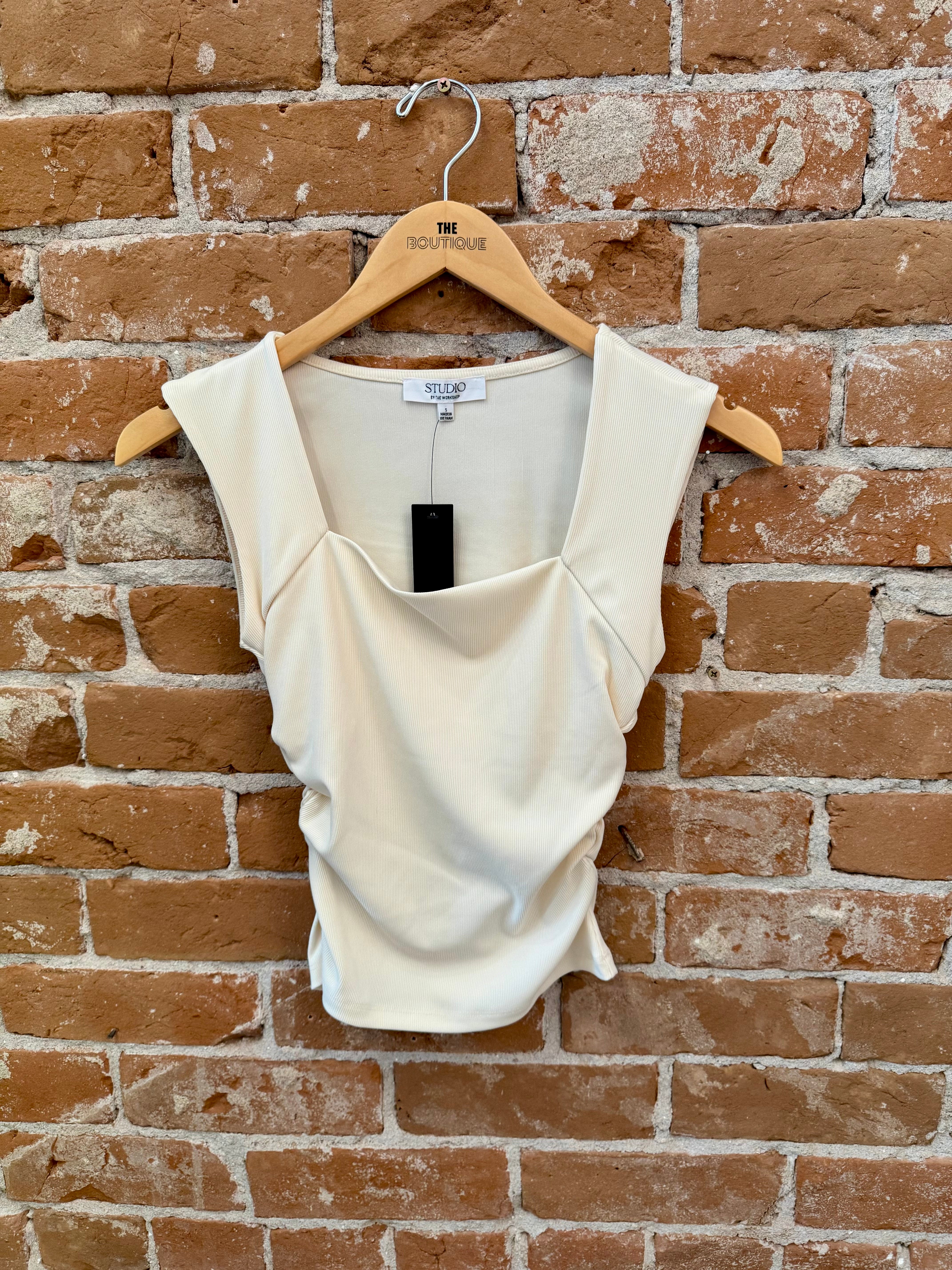 White sleeveless top on a hanger against a brick wall