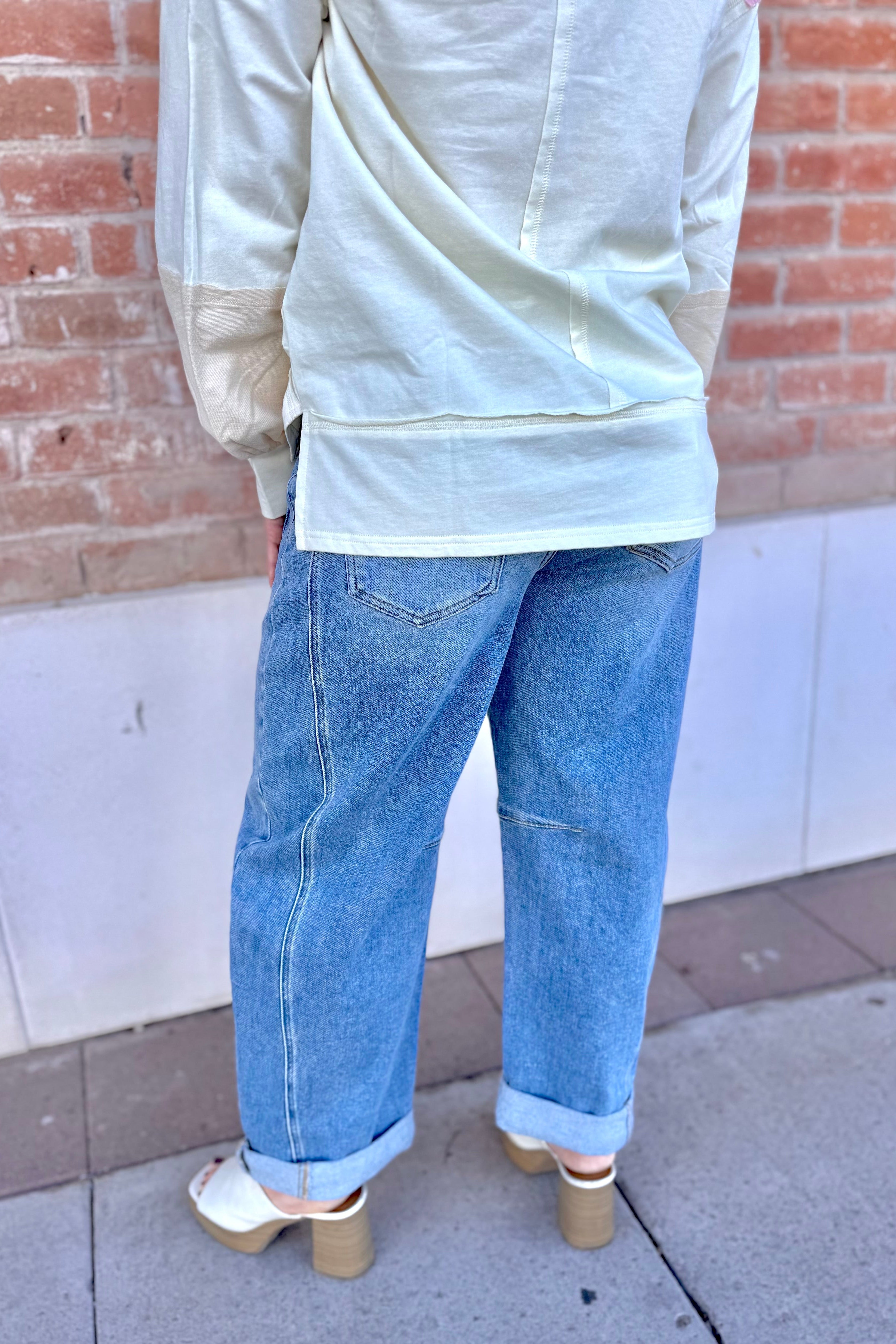 Person wearing a light-colored top and blue jeans standing against a brick wall.
