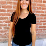Woman wearing a black t-shirt and blue jeans standing in front of a brick wall.