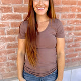 Woman wearing a brown t-shirt and blue jeans standing against a brick wall.
