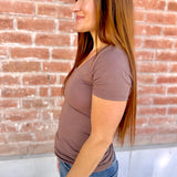 Woman wearing a brown t-shirt and blue jeans standing against a brick wall.