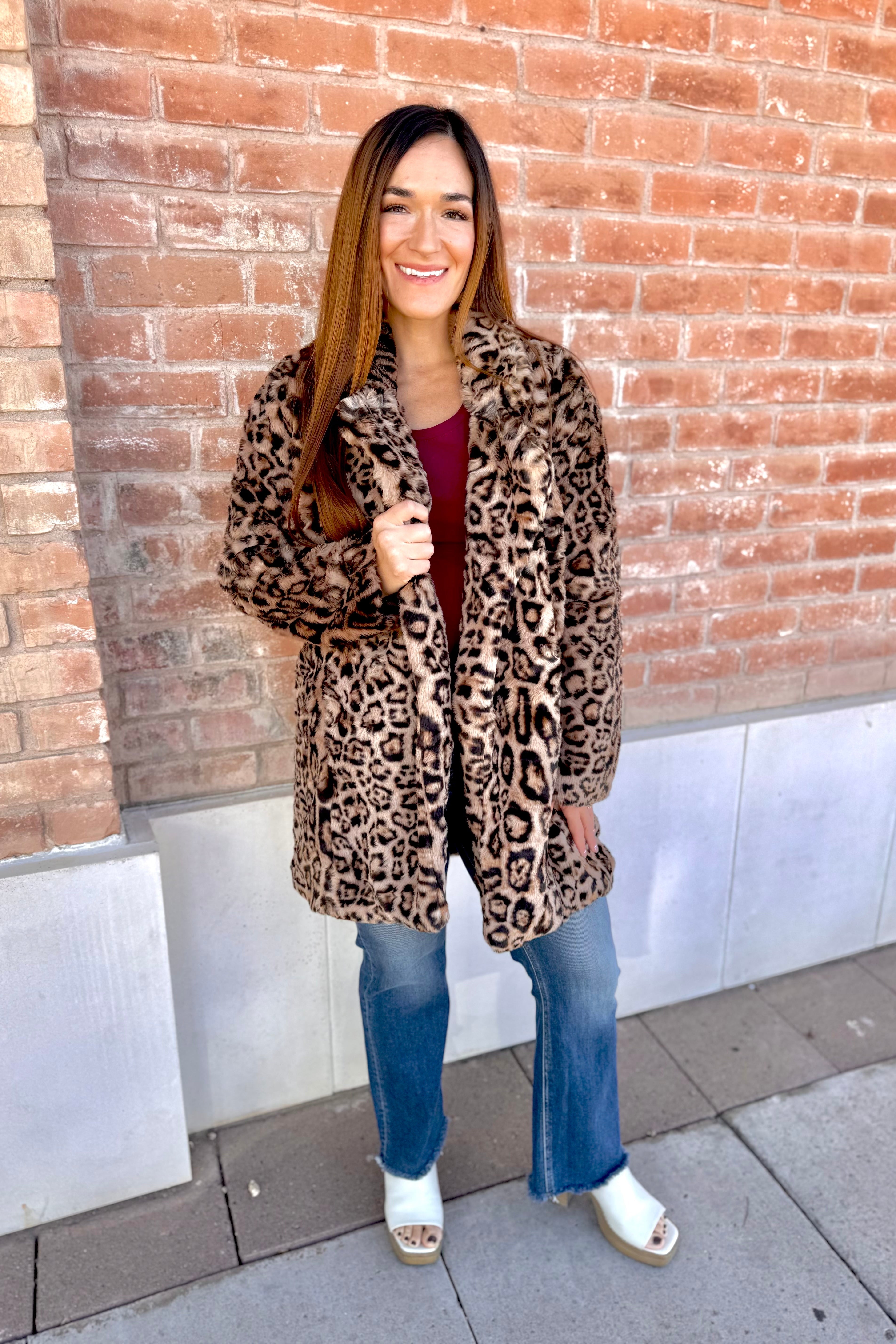 Woman wearing a leopard print coat standing against a brick wall.