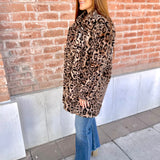 Woman wearing a leopard print coat standing against a brick wall.