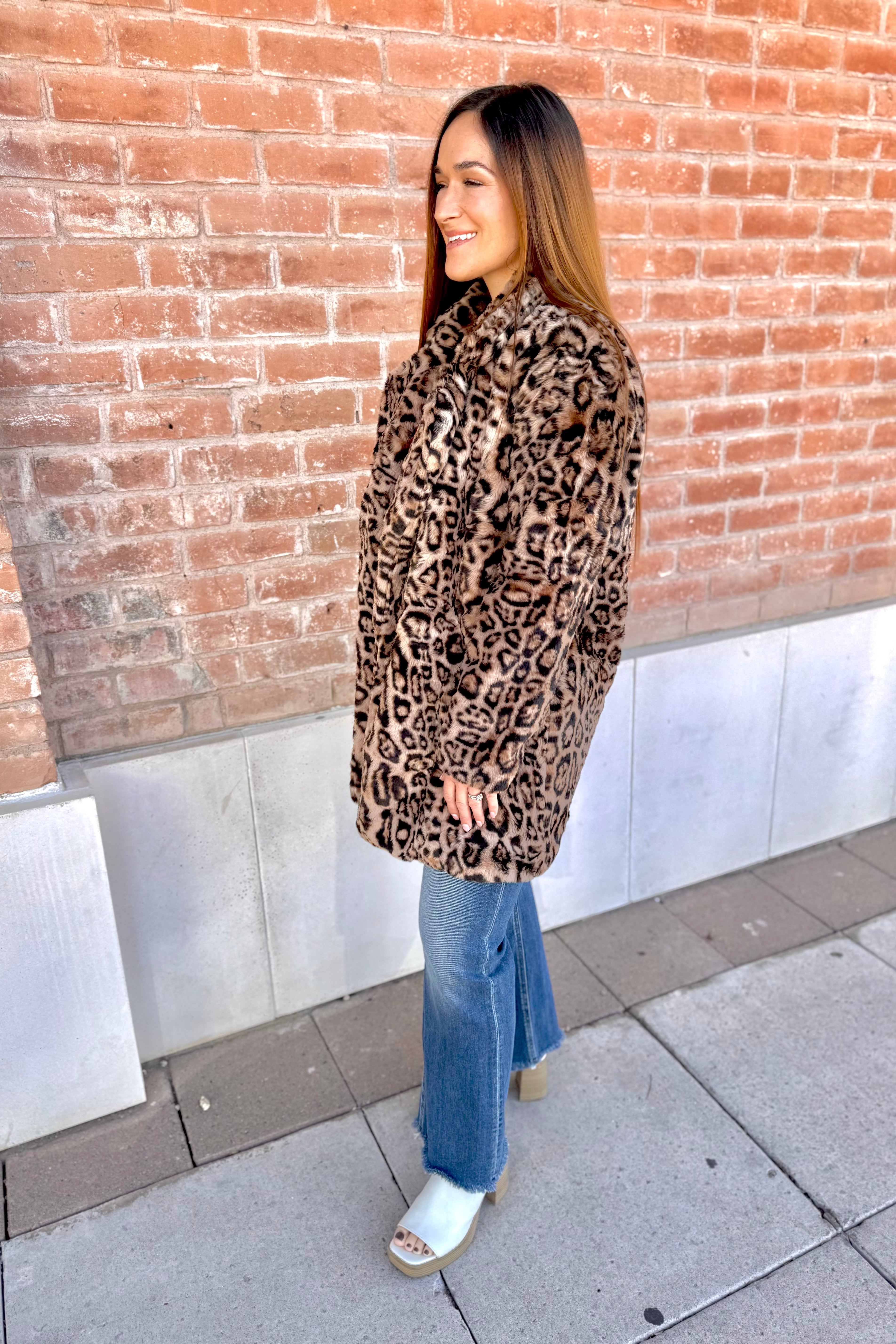 Woman wearing a leopard print coat standing against a brick wall.