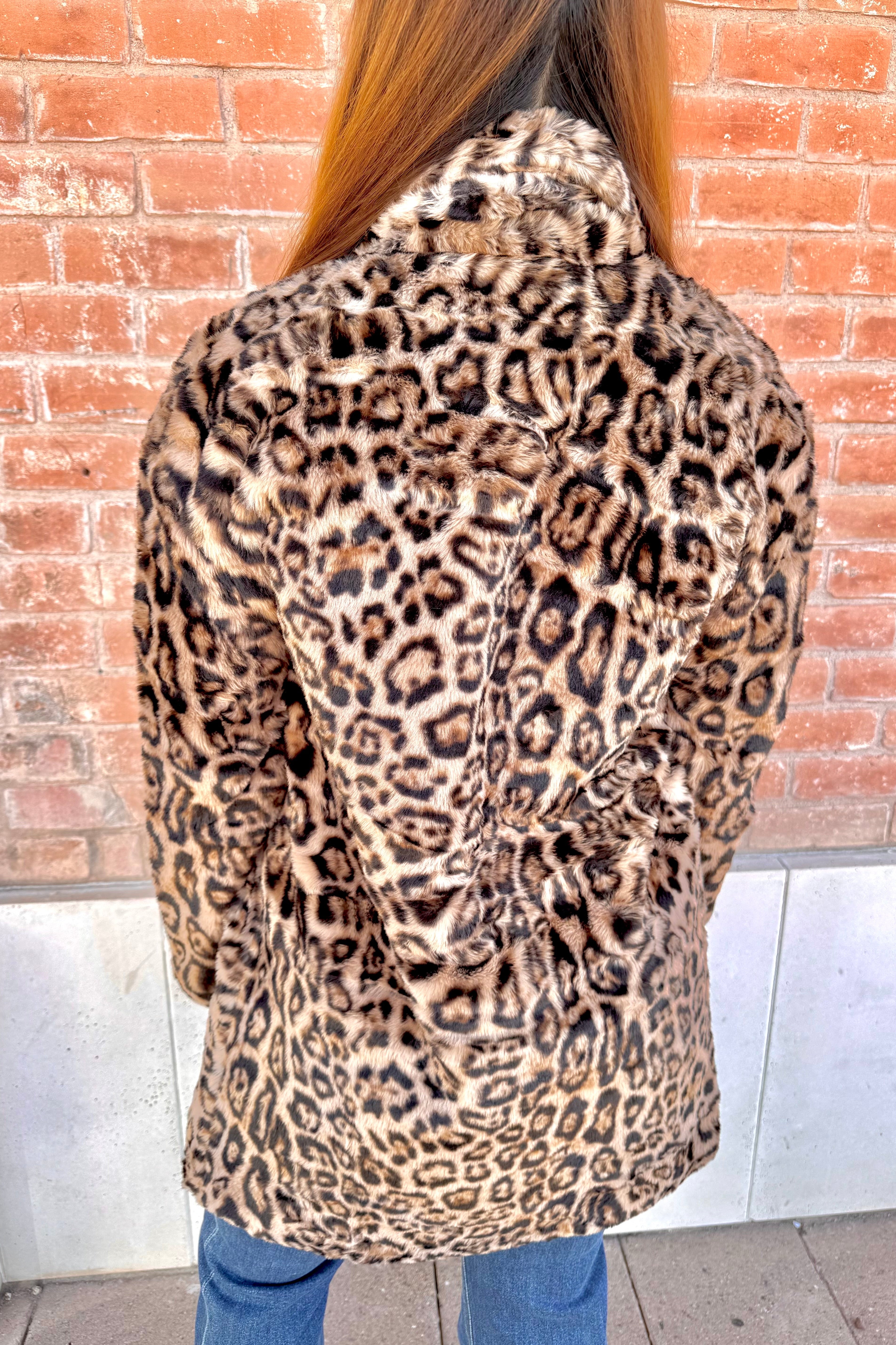 Person wearing a leopard print coat with a brick wall background