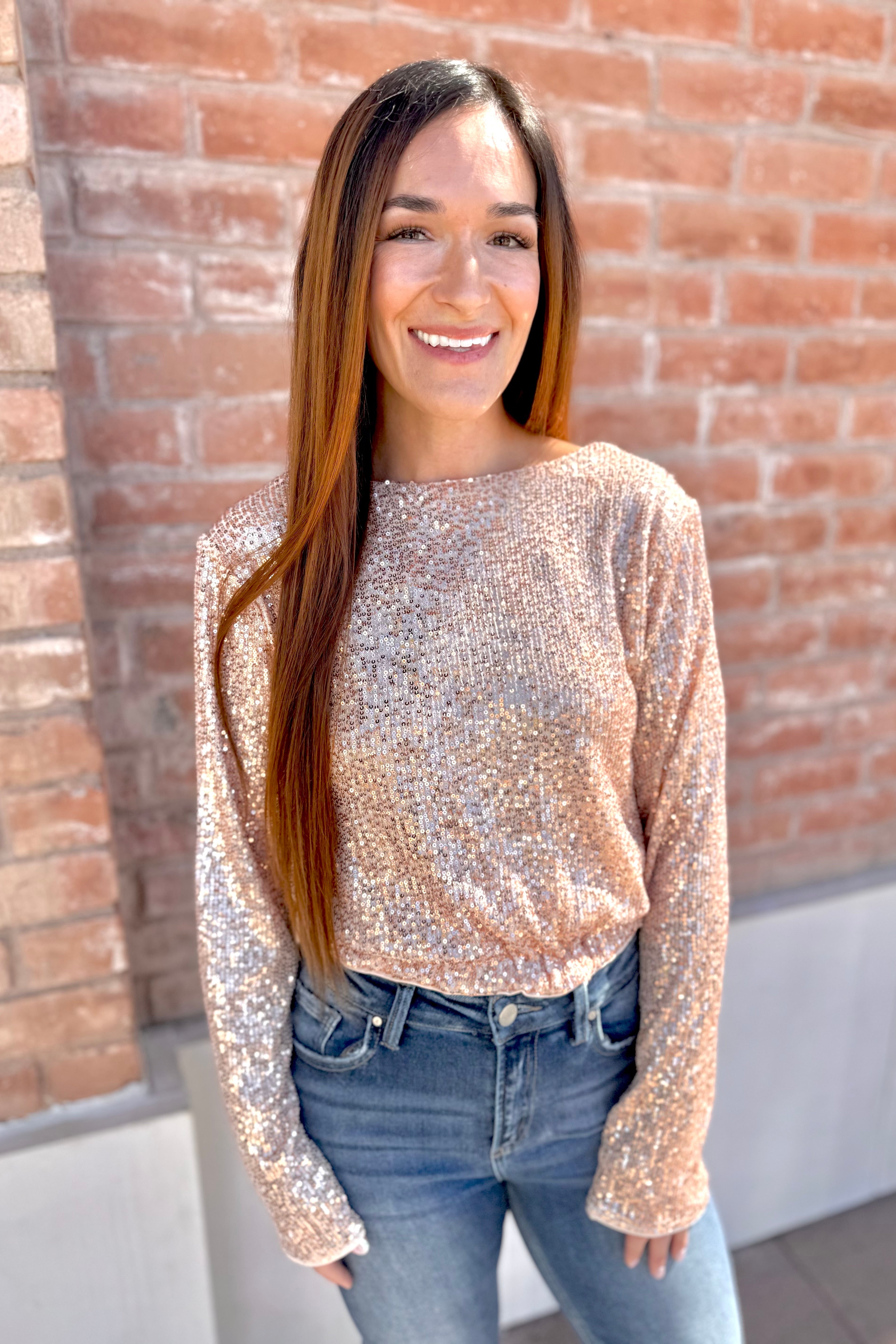 Woman wearing a sparkly top and jeans standing against a brick wall.