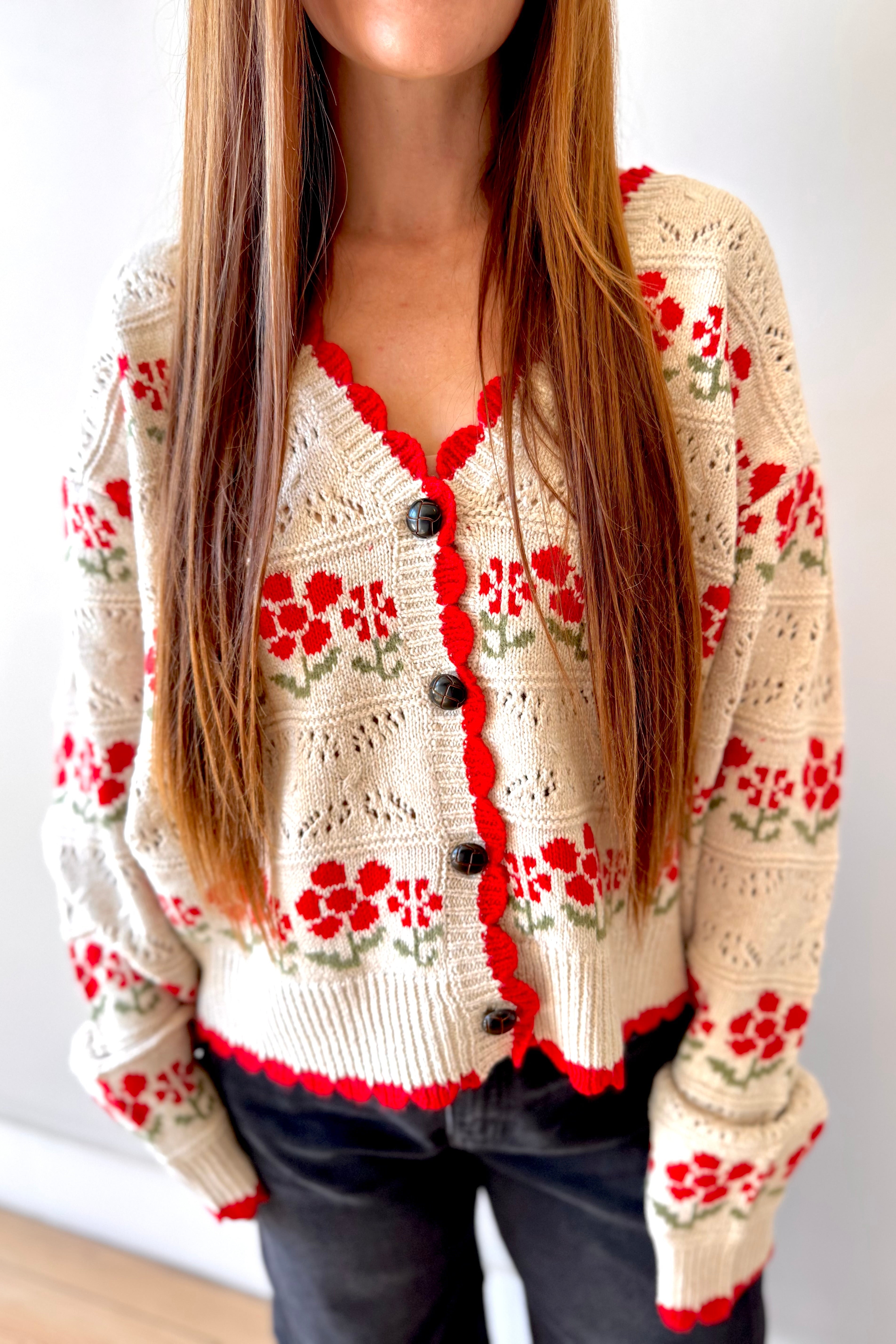 Person wearing a cream-colored cardigan with red floral patterns on a white background