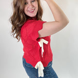 Woman wearing a red sweater with a white bow and blue jeans against a plain background