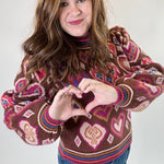 Person wearing a patterned sweater making a heart shape with their hands on a plain background