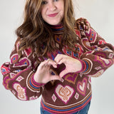 Person wearing a patterned sweater making a heart shape with their hands on a plain background