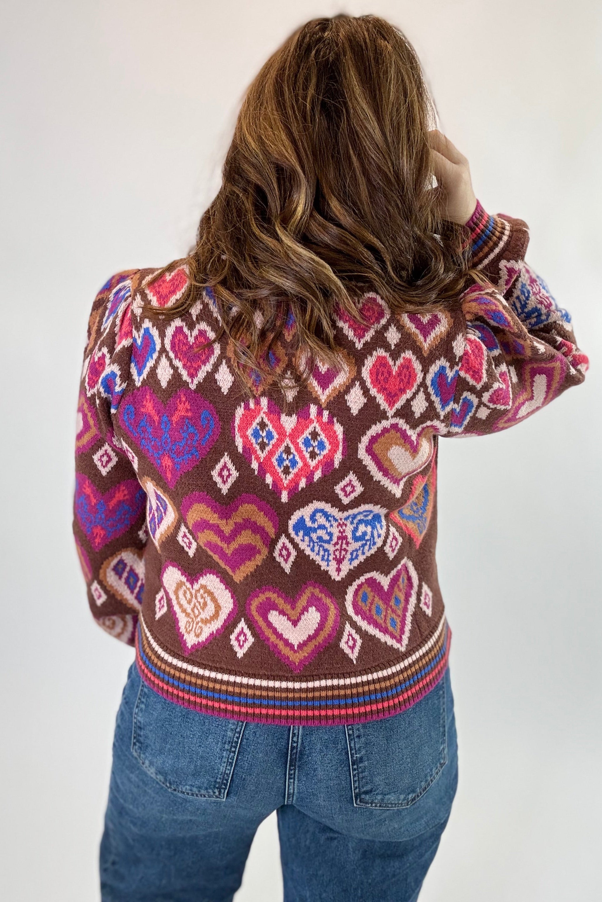 Person wearing a sweater with heart pattern on a plain background