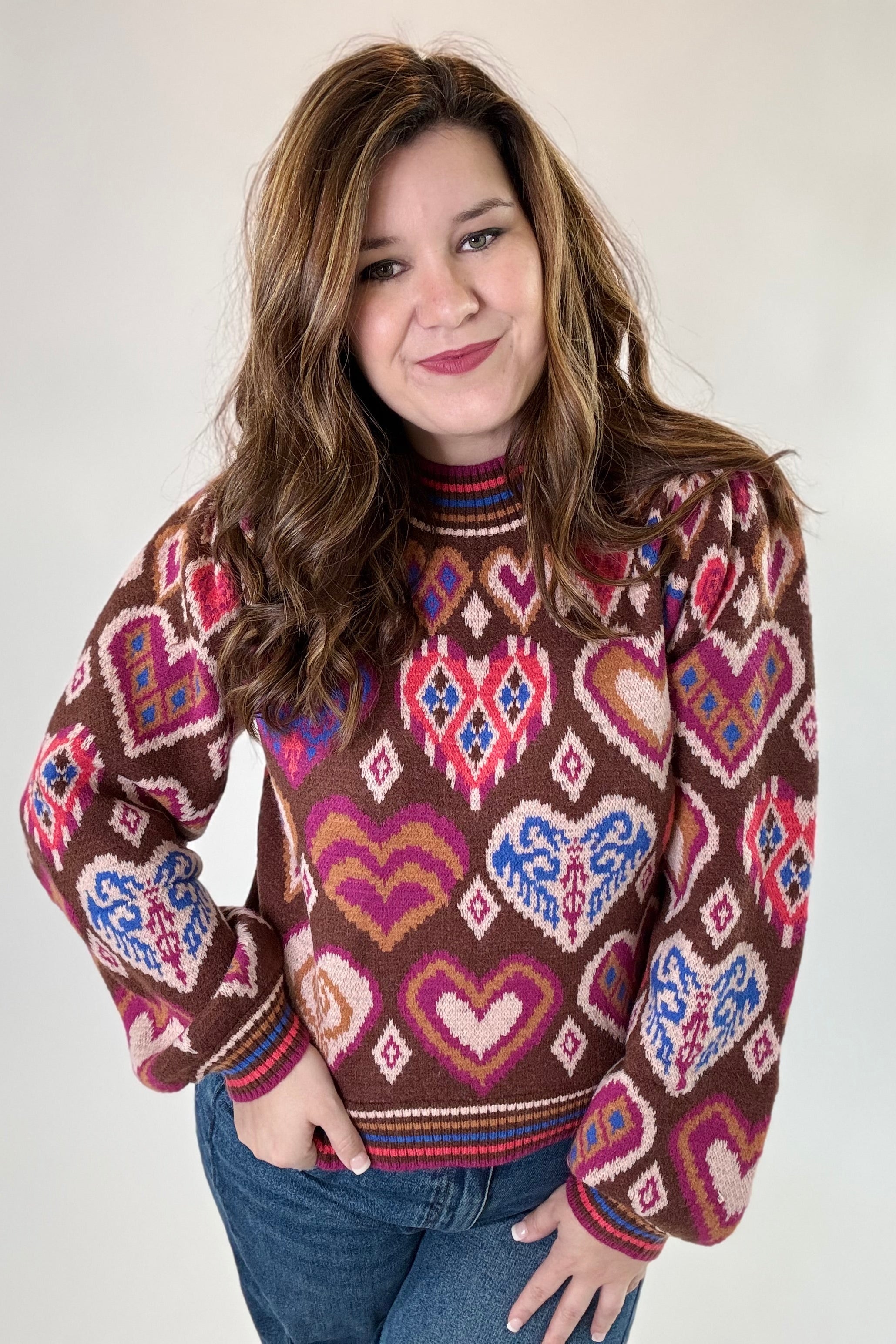 Woman wearing a patterned sweater with hearts and abstract designs on a plain background