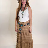 Woman wearing a long brown skirt with buttons, a white top, and a hat on a white background