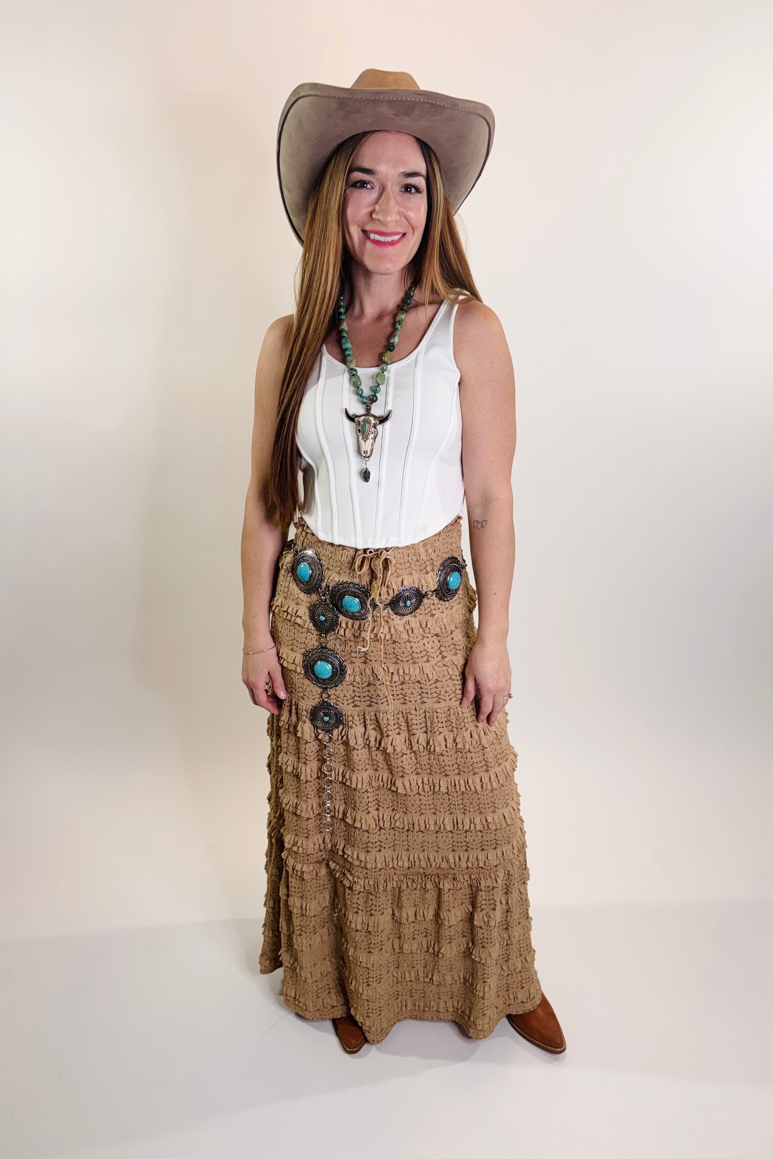 Woman wearing a long brown skirt with buttons, a white top, and a hat on a white background