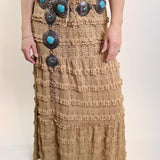 Person wearing a long, textured brown skirt with decorative buttons on a plain background