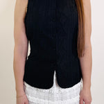 Person wearing a black sleeveless top and white ruffled skirt on a plain background