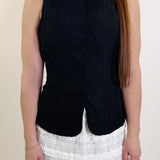 Person wearing a black sleeveless top and white ruffled skirt on a plain background