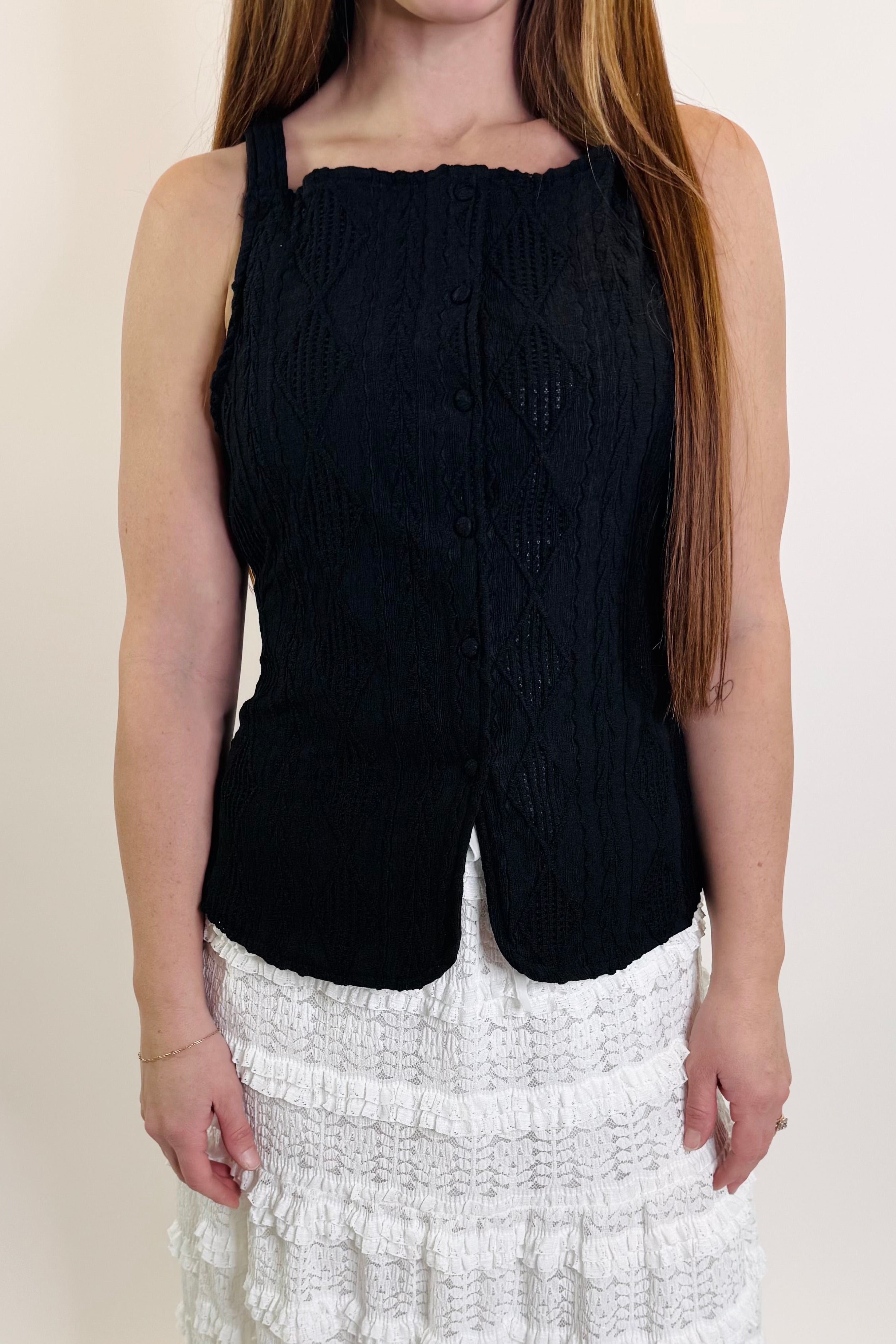 Person wearing a black sleeveless top and white ruffled skirt on a plain background