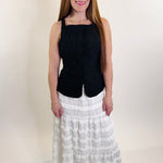 Woman wearing a black top and white patterned skirt on a plain background