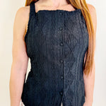 Person wearing a dark blue knitted sleeveless top with button details on a beige background