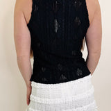 Person wearing a black sleeveless top and white skirt on a plain background