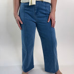 Person wearing blue jeans standing against a white wall