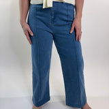 Person wearing blue jeans standing against a white wall